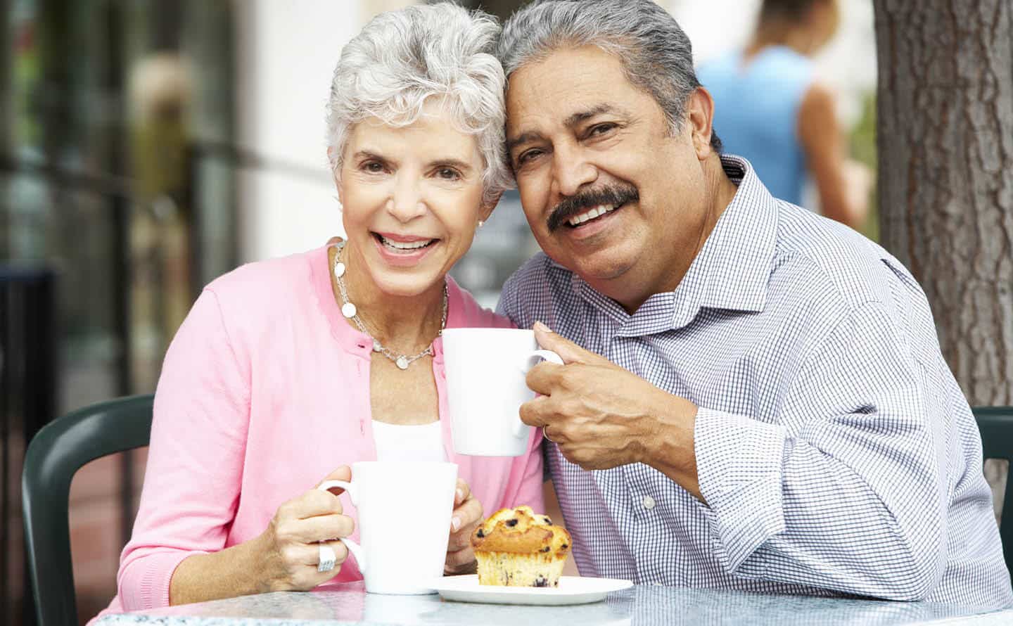 Senior couple enjoying coffee and muffins outdoors.