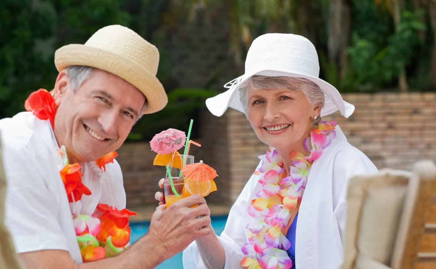 Senior couple in hats, leis and fruity drinks by pool