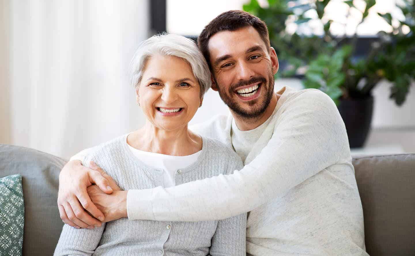 Senior mother and son embracing on a grey couch