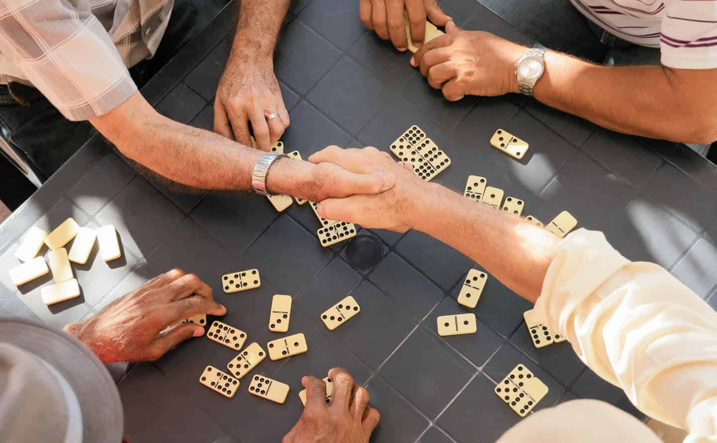 A group of four people playing dominos; two of the players are shaking hands.