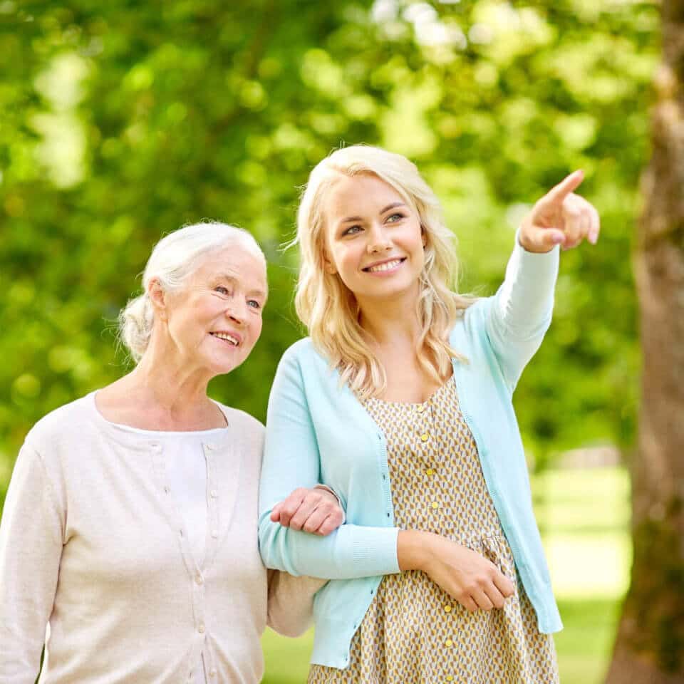 Senior woman walking arm in arm with her daughter outside.