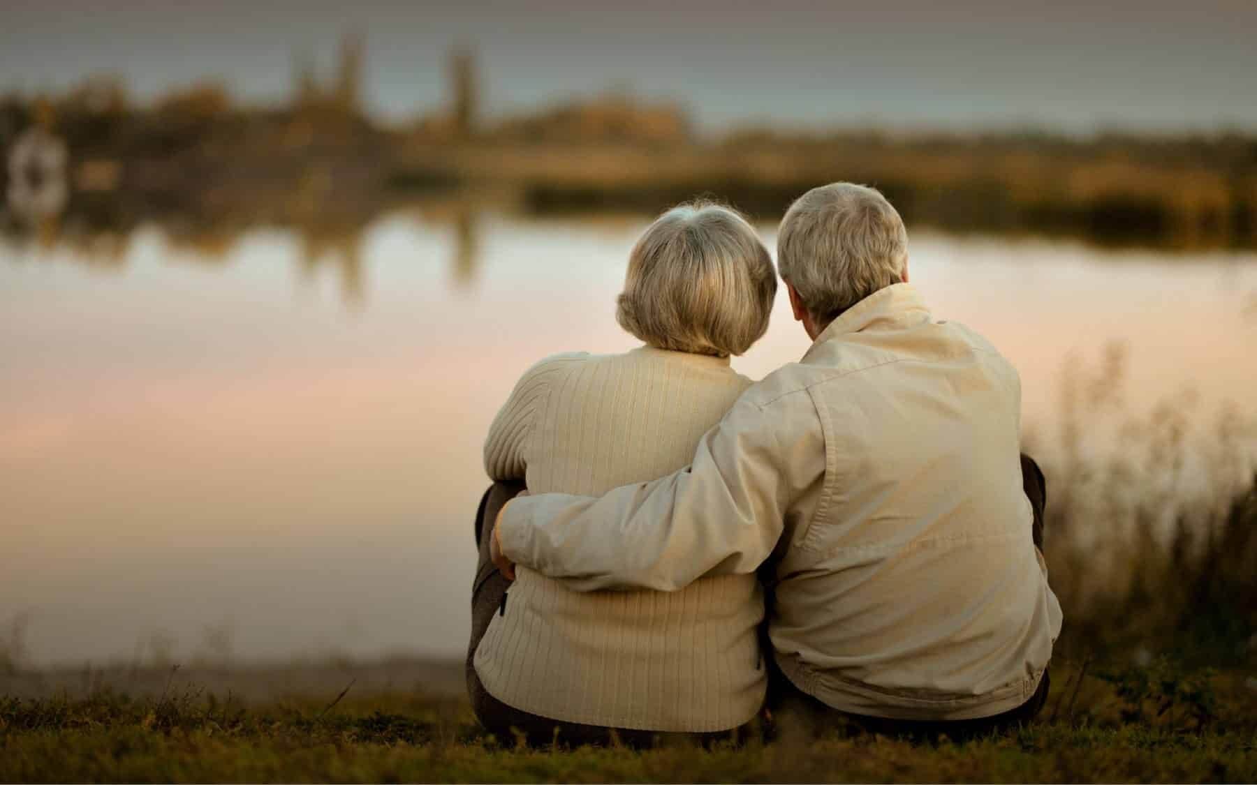 A senior couple enjoying a lake view with arms around each other.