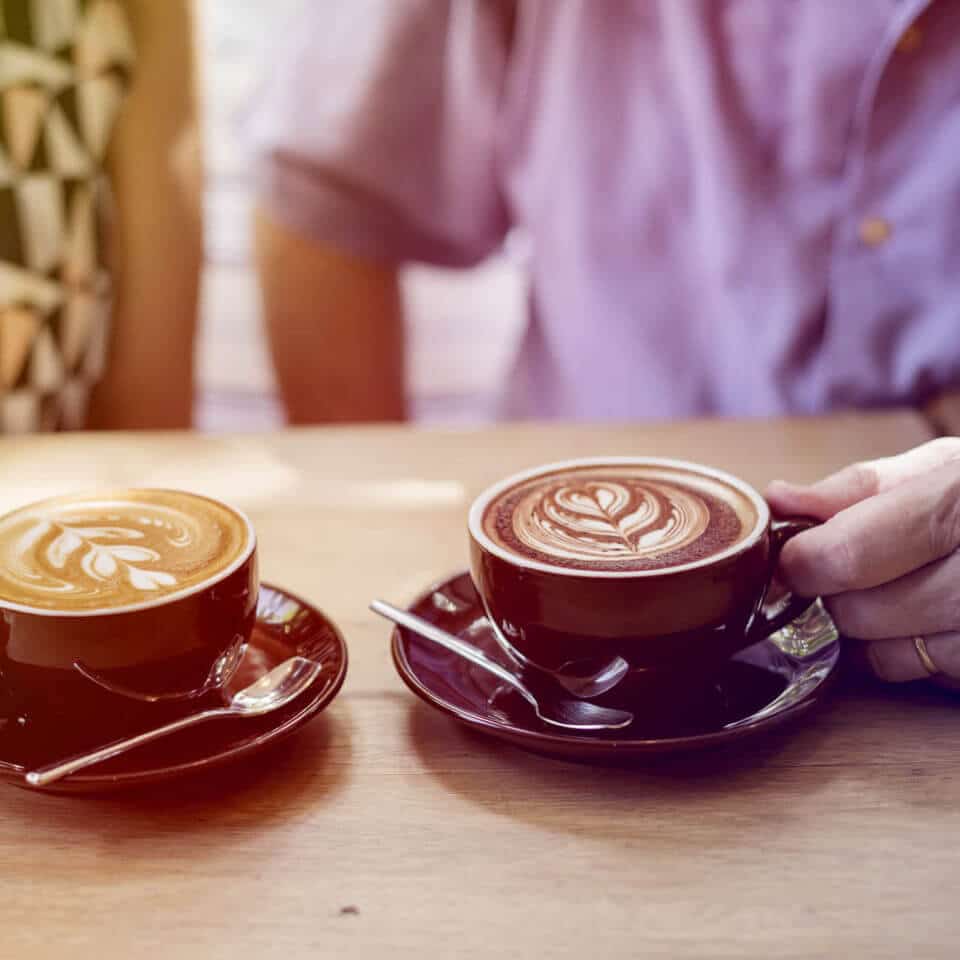 Two people out of focus enjoying lattes together.